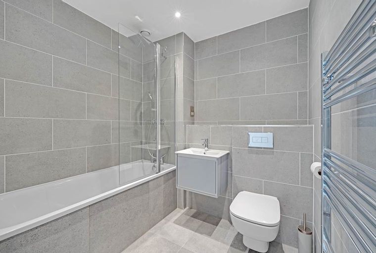 A bathroom with a bathtub, shower screen, sink, toilet, and heated towel rail.