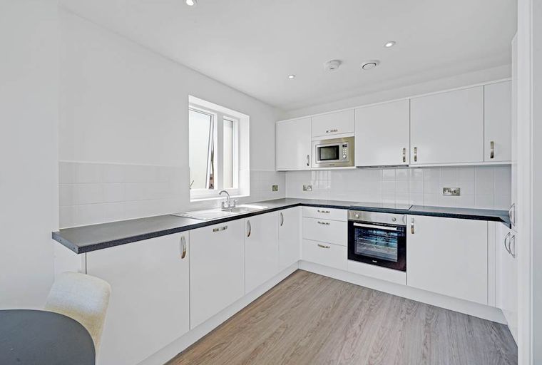 A modern kitchen with white cabinets, a dark countertop, a sink, and an oven.