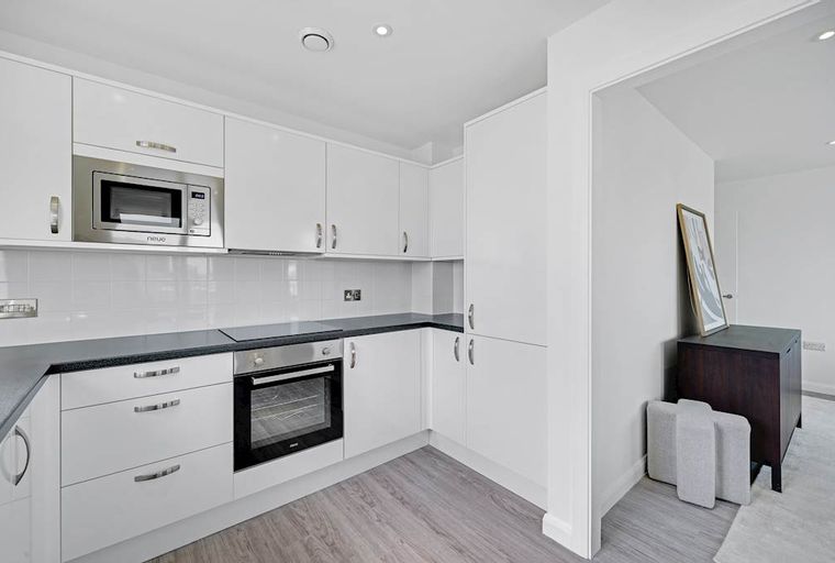 A modern kitchen with white cabinets, a microwave, an oven, and a dark countertop.