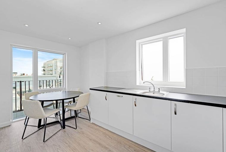 A kitchen and dining area with a round table, chairs, white cabinets, and a sink.