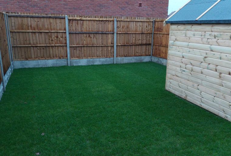 A backyard with a lawn, wooden fence, and a shed.