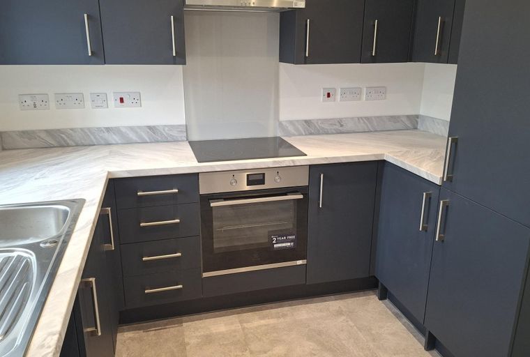 A modern kitchen with dark grey cabinets, a marble-effect countertop, an oven, and a hob.