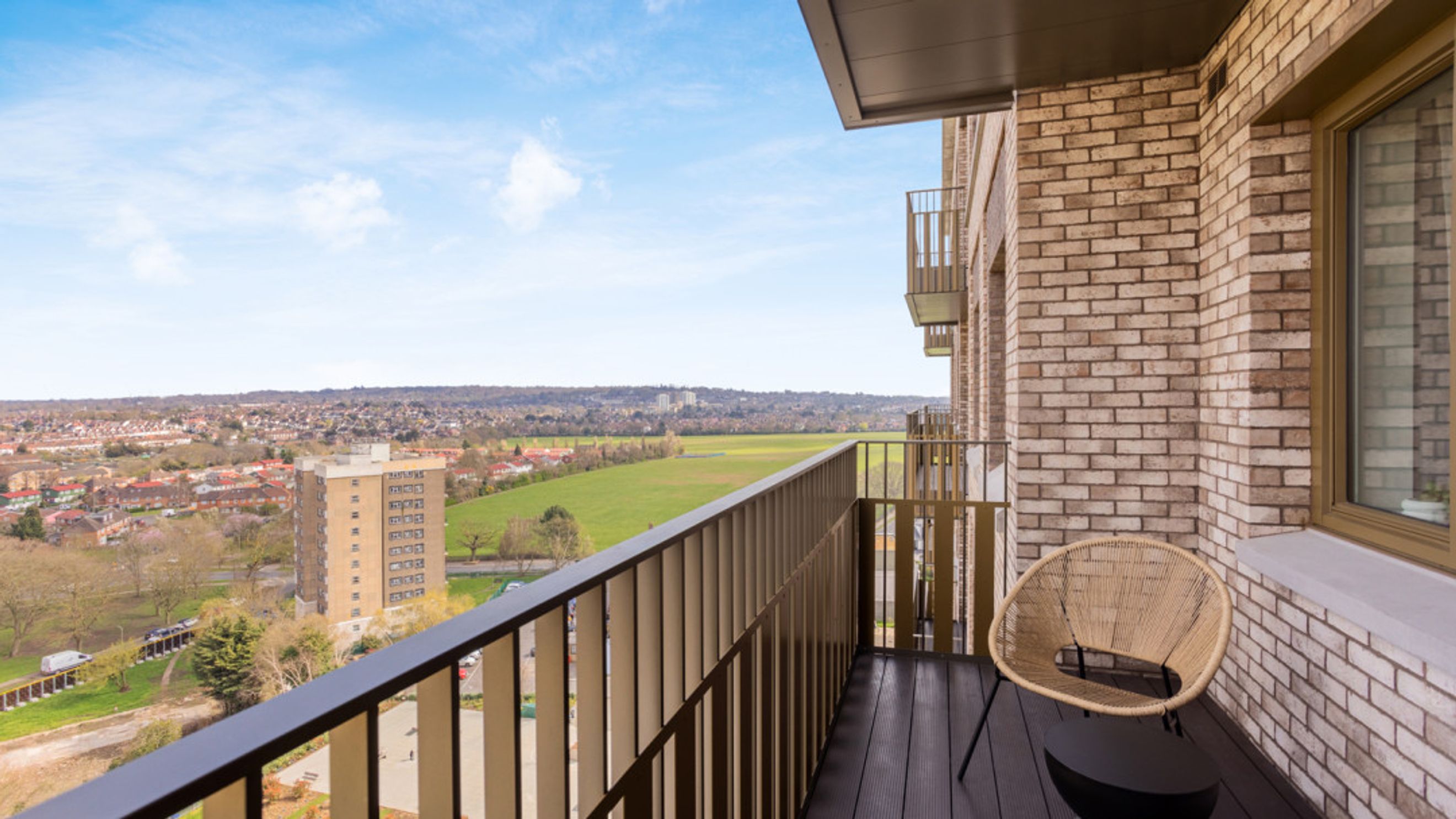 A balcony with a chair and a view of a cityscape and a field.