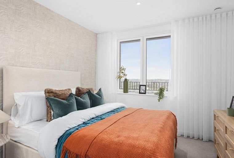 A bedroom with a bed, pillows, a throw blanket, a window, and a dresser.