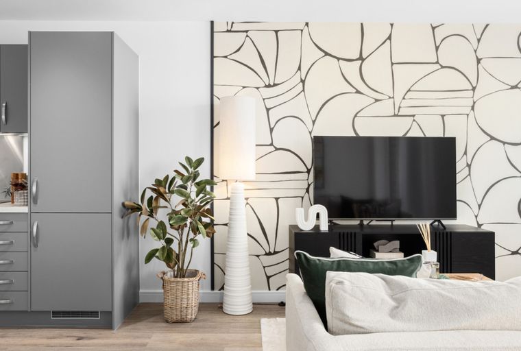 A living room and kitchen area with a sofa, television, and kitchen cabinets.