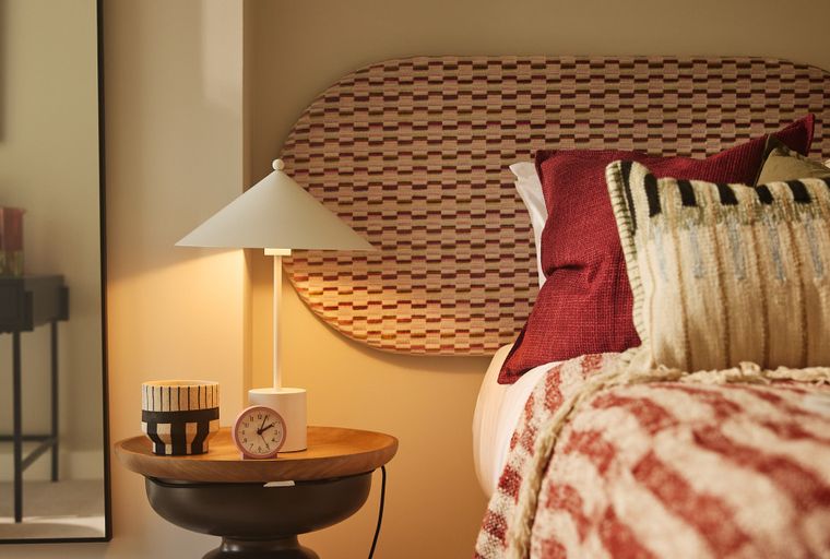 A bedroom with a bed, pillows, a headboard, a bedside table, and a lamp.