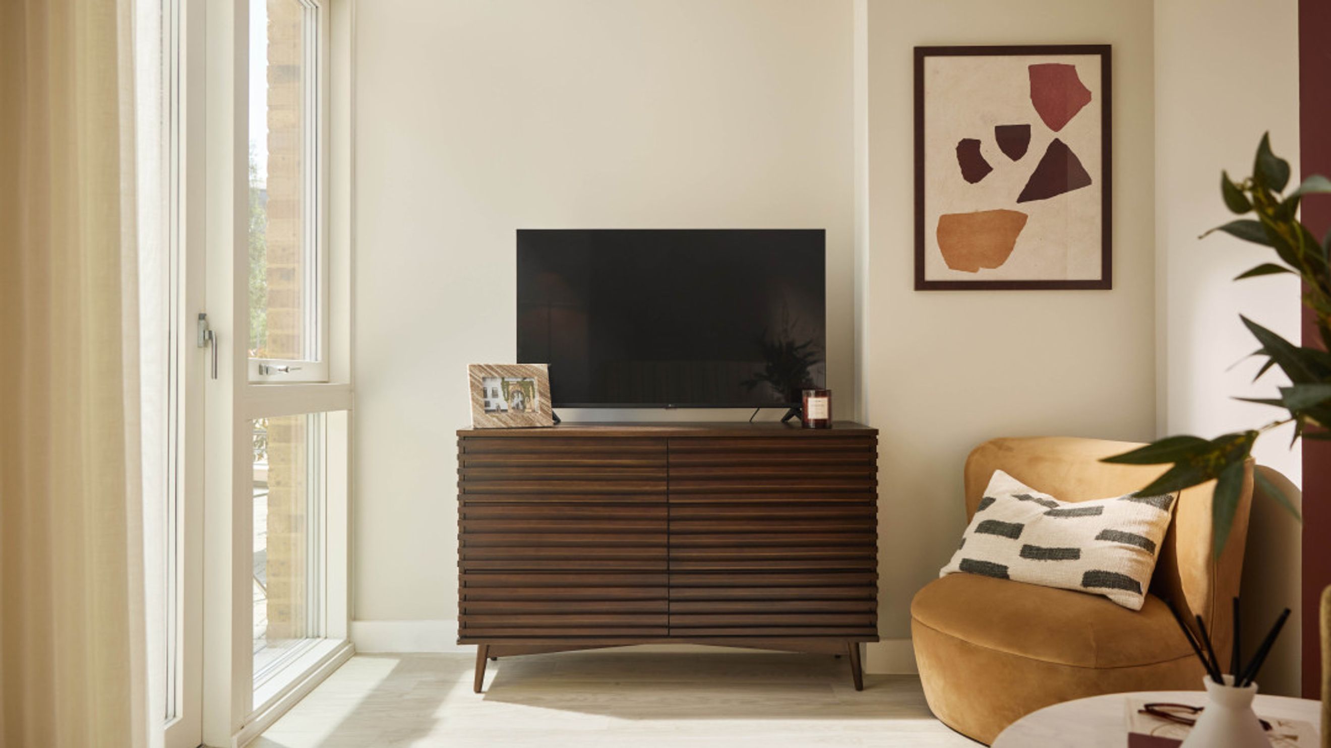 A living room with a television on a wooden cabinet and a chair with a pillow.