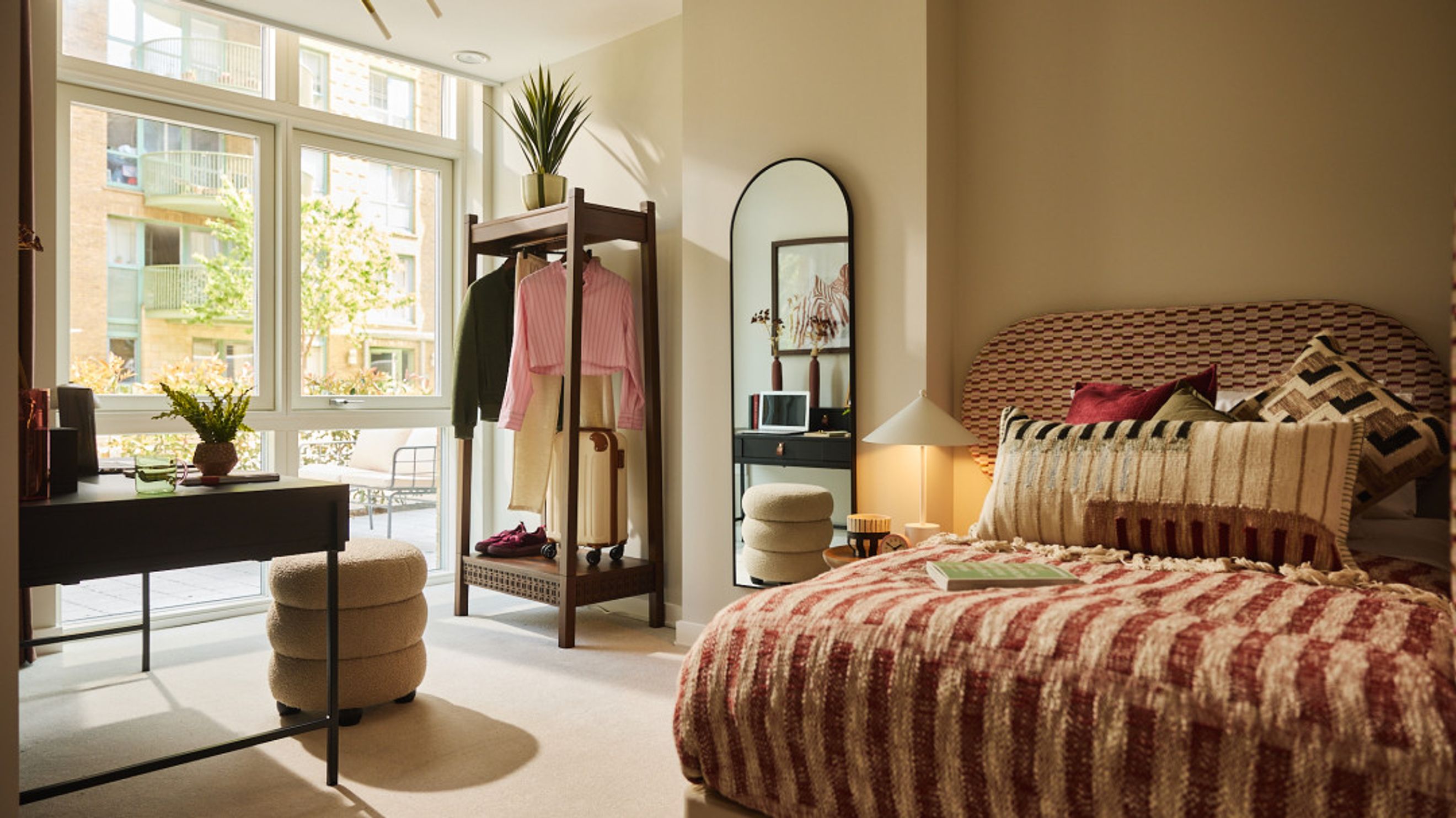 A bedroom with a bed, a clothing rack, a vanity, and a large window.