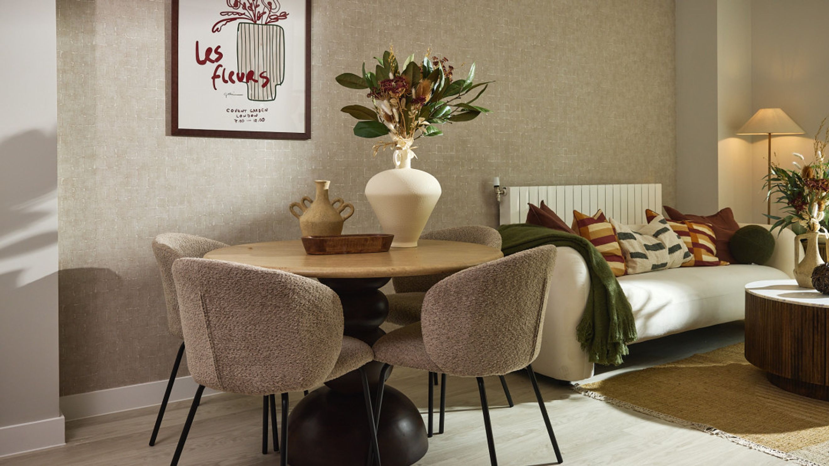 A dining area with a round table and chairs next to a sofa with pillows and a lamp.