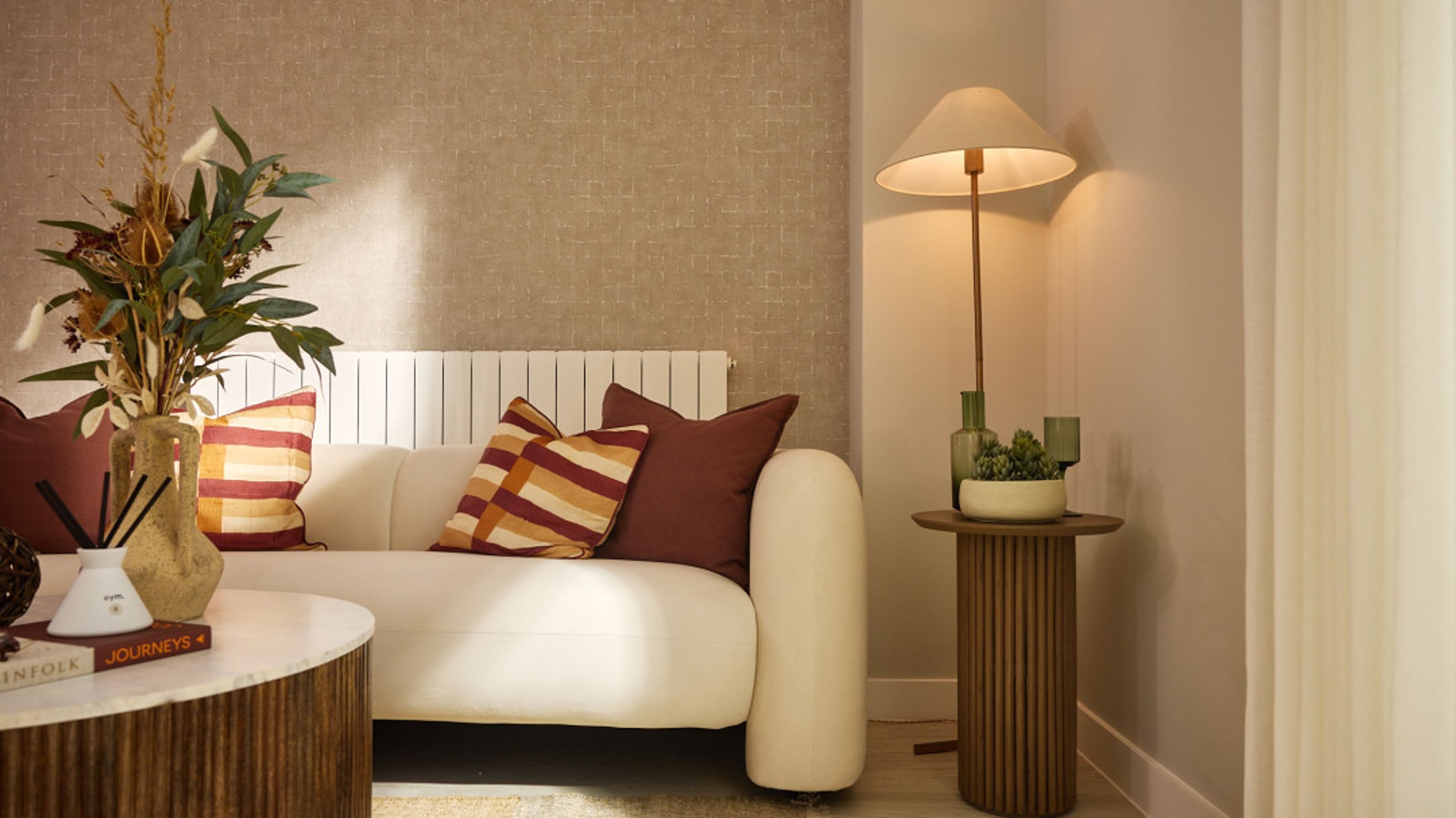 A living room with a white sofa, accent pillows, a dried floral arrangement, and a floor lamp.