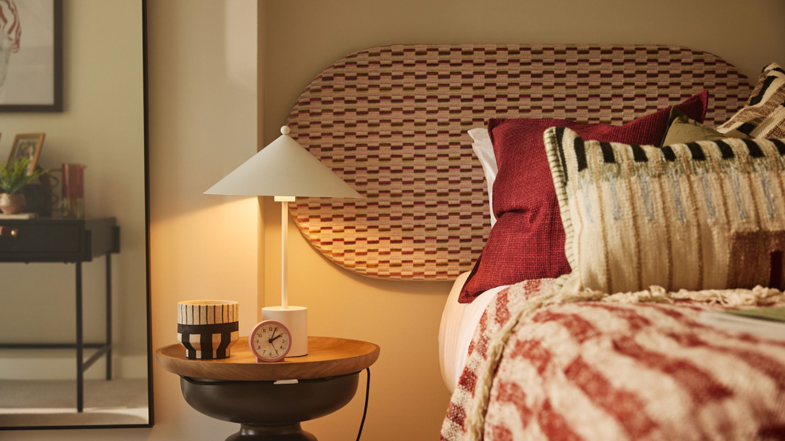 A bedroom with a bed, pillows, a headboard, a bedside table, and a lamp.