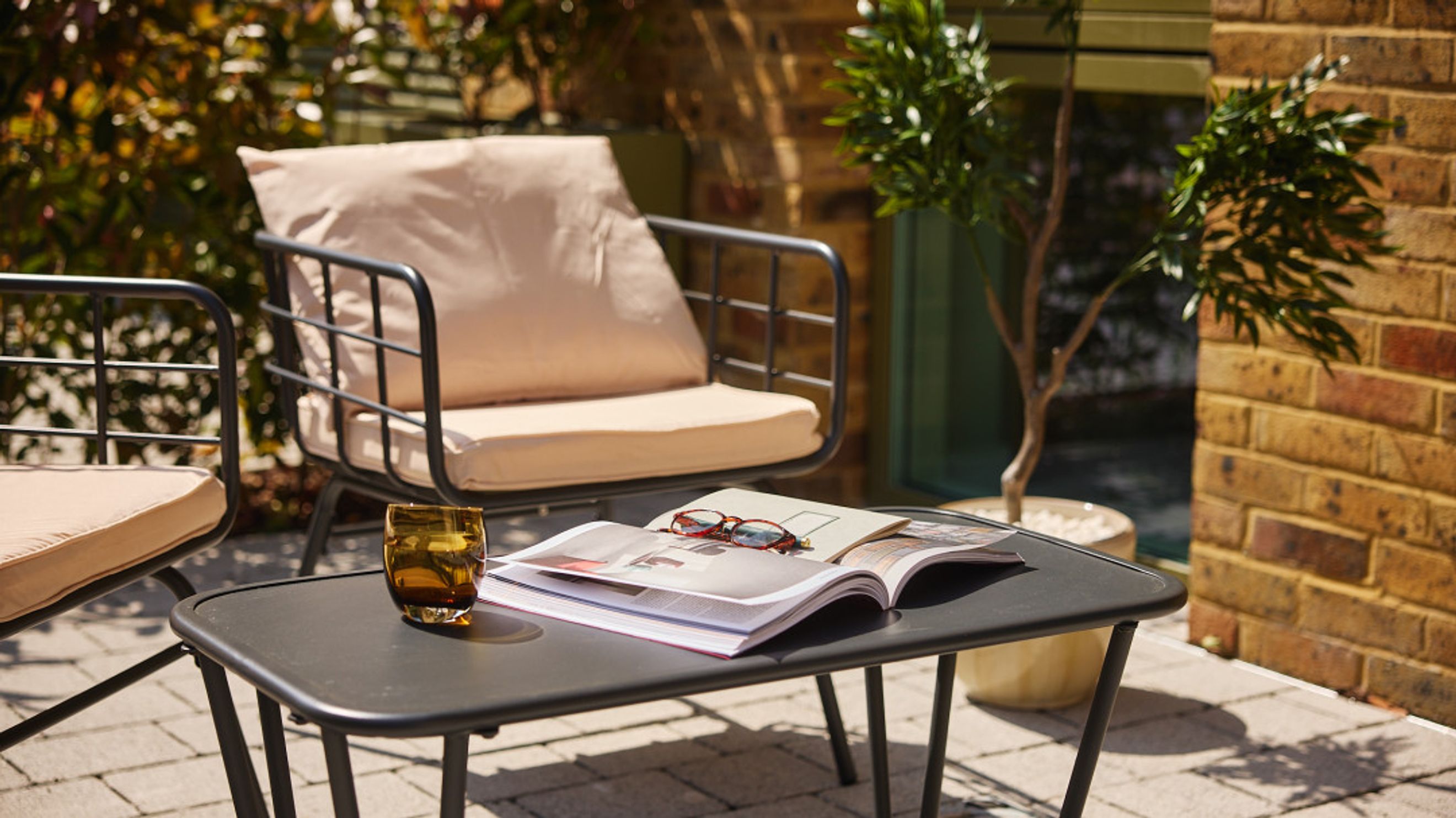 A patio seating area with two chairs, a coffee table, a glass, and an open book.