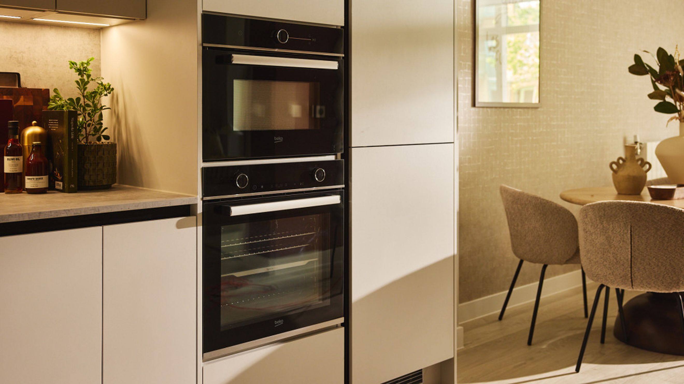 A modern kitchen with integrated ovens and a dining area with chairs and a table.