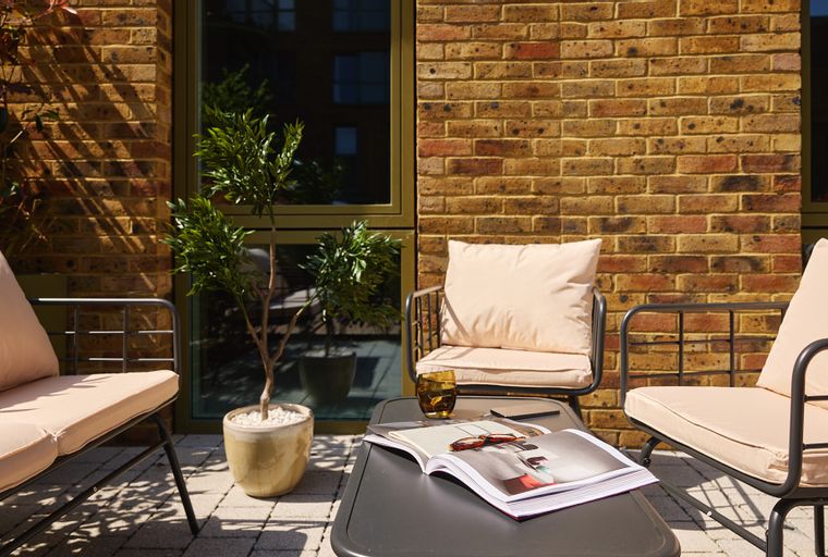 A patio with two chairs, a coffee table, and a potted plant.