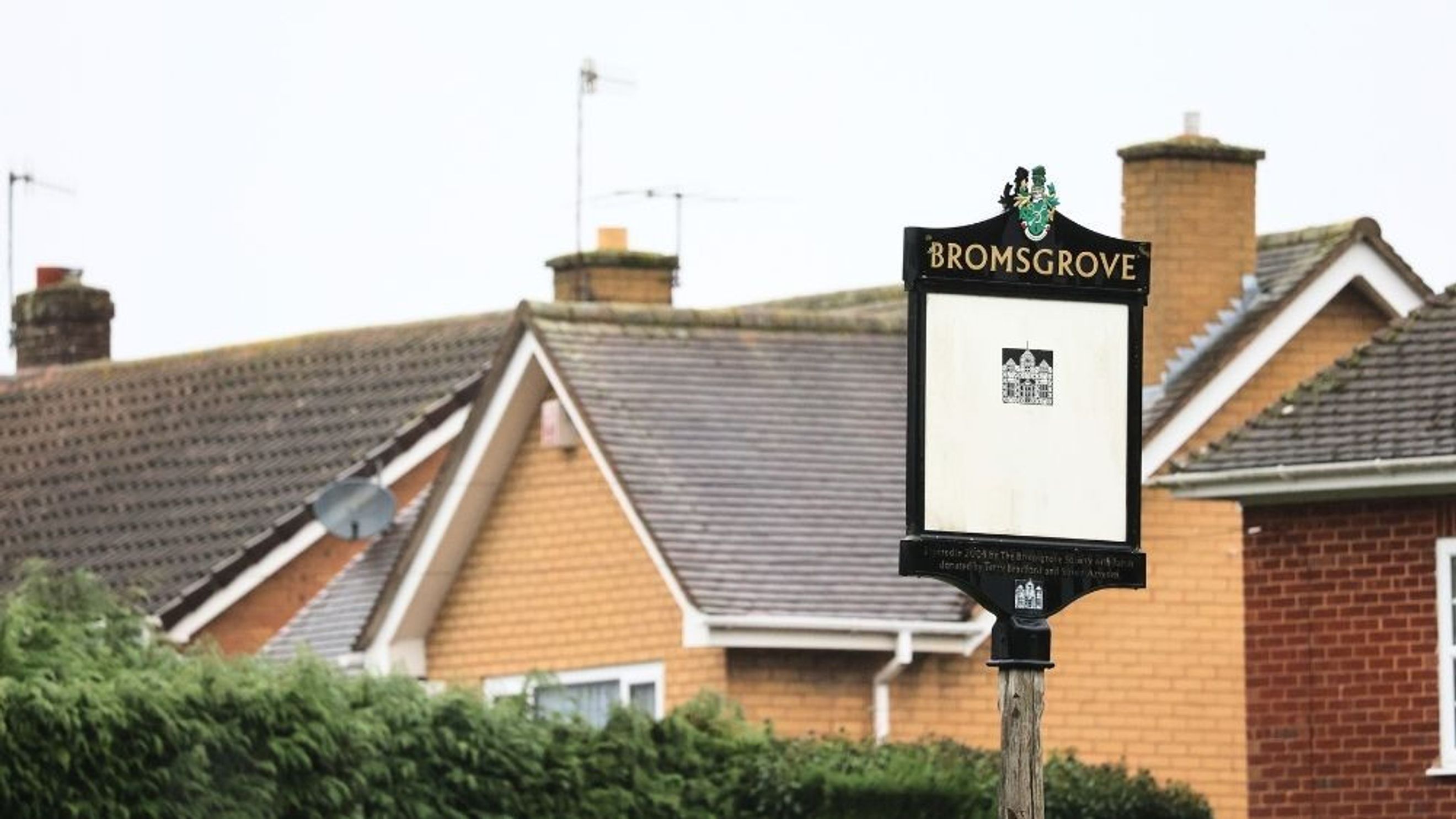 A Bromsgrove town signpost stands in front of houses with tiled roofs.
