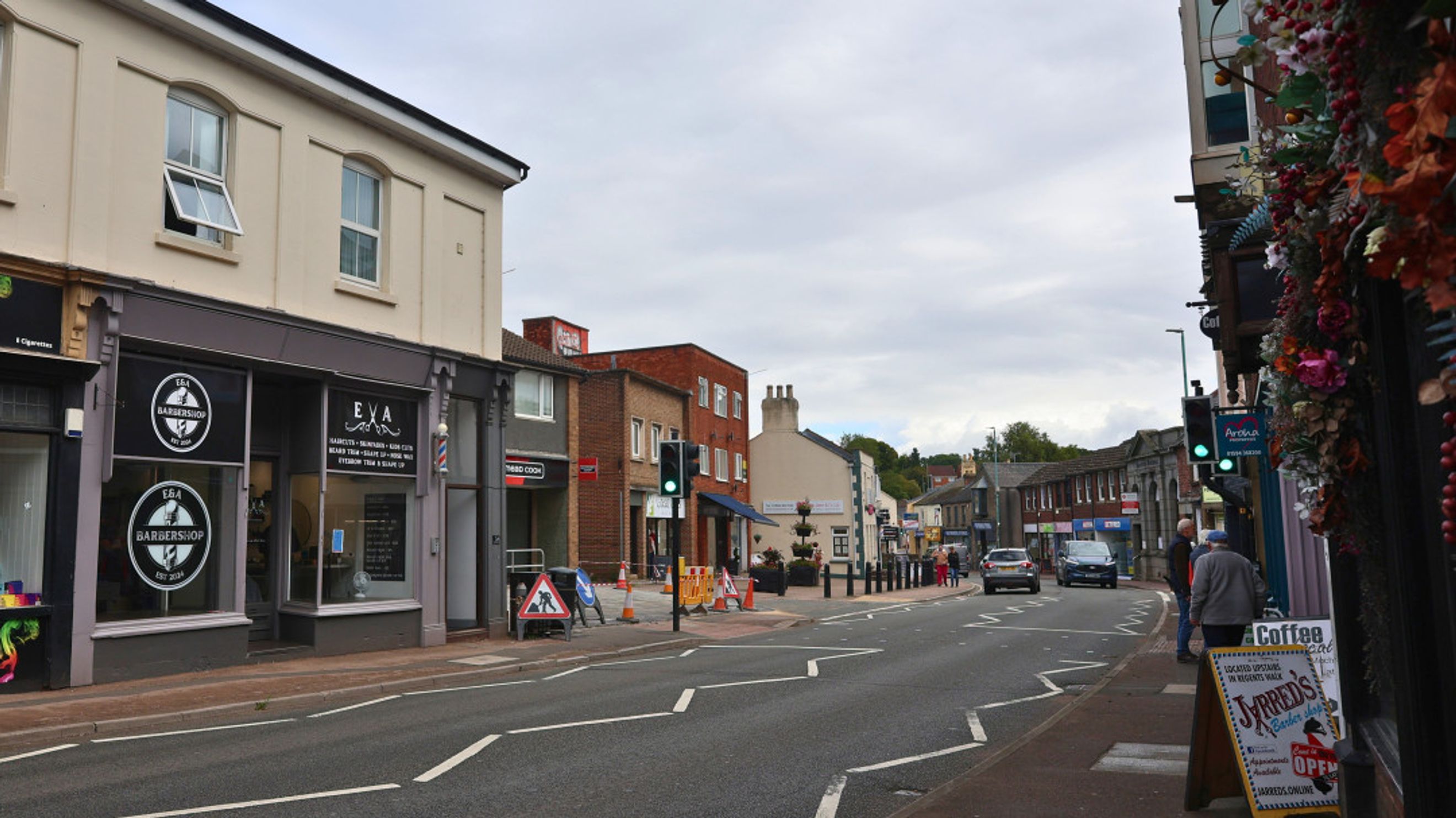 A street scene with various shops and businesses, including barbershops, on a cloudy day.