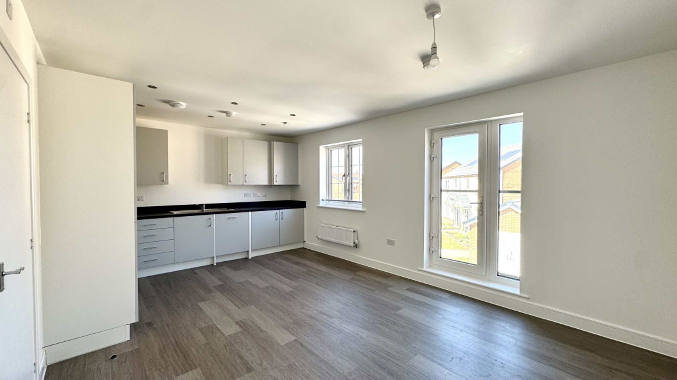 A kitchen and living area with cabinets, a sink, windows, and French doors.