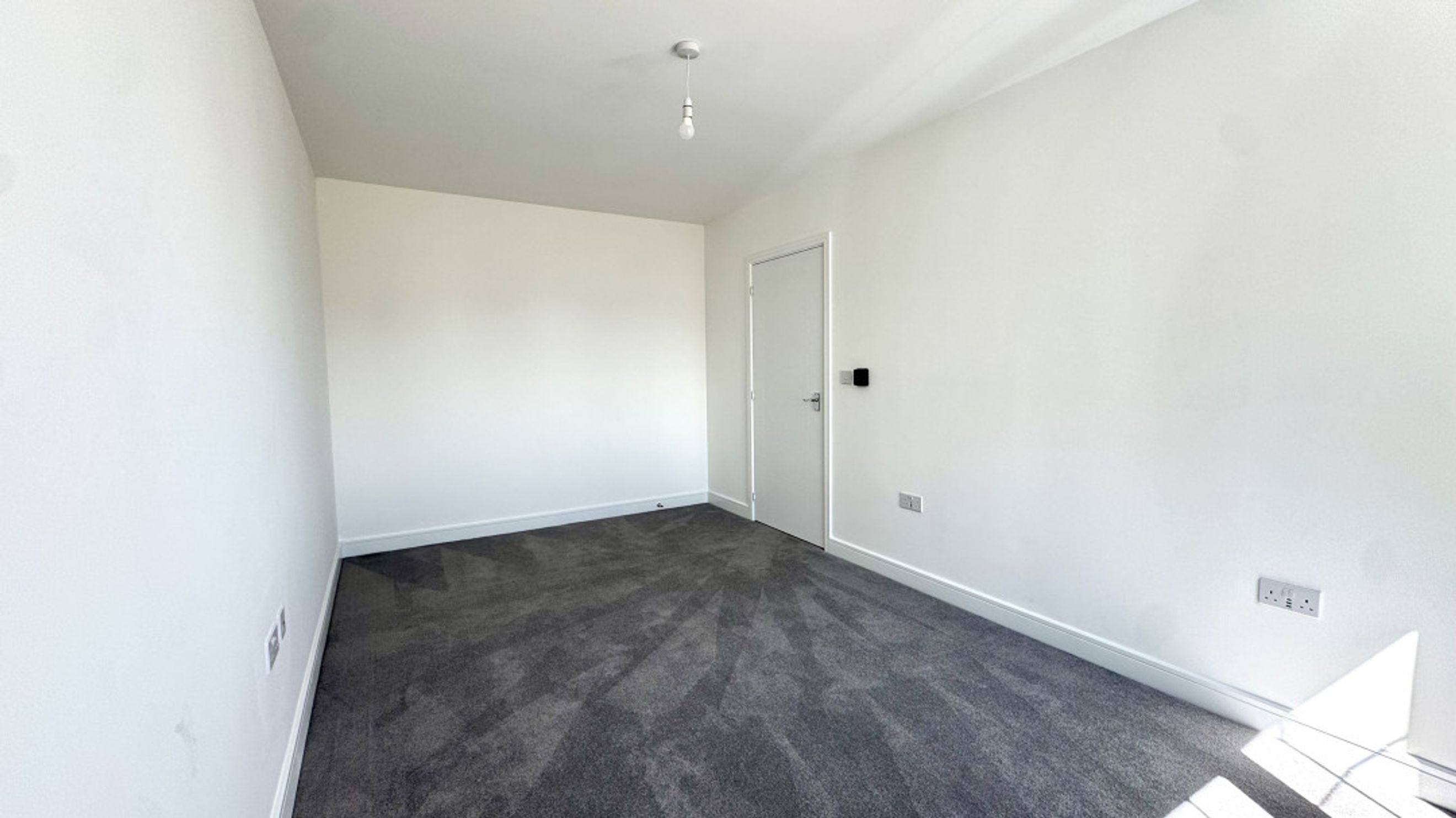 A room with grey carpet, white walls, and a white door.