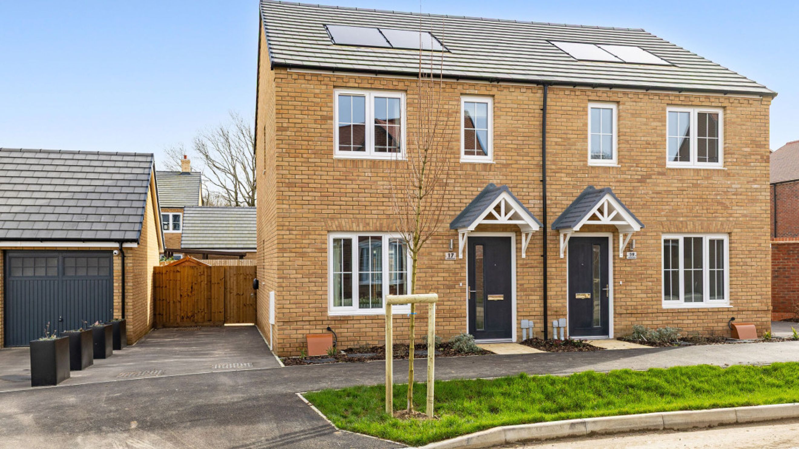 A new-build semi-detached house with a brick facade, grey garage, and driveway.