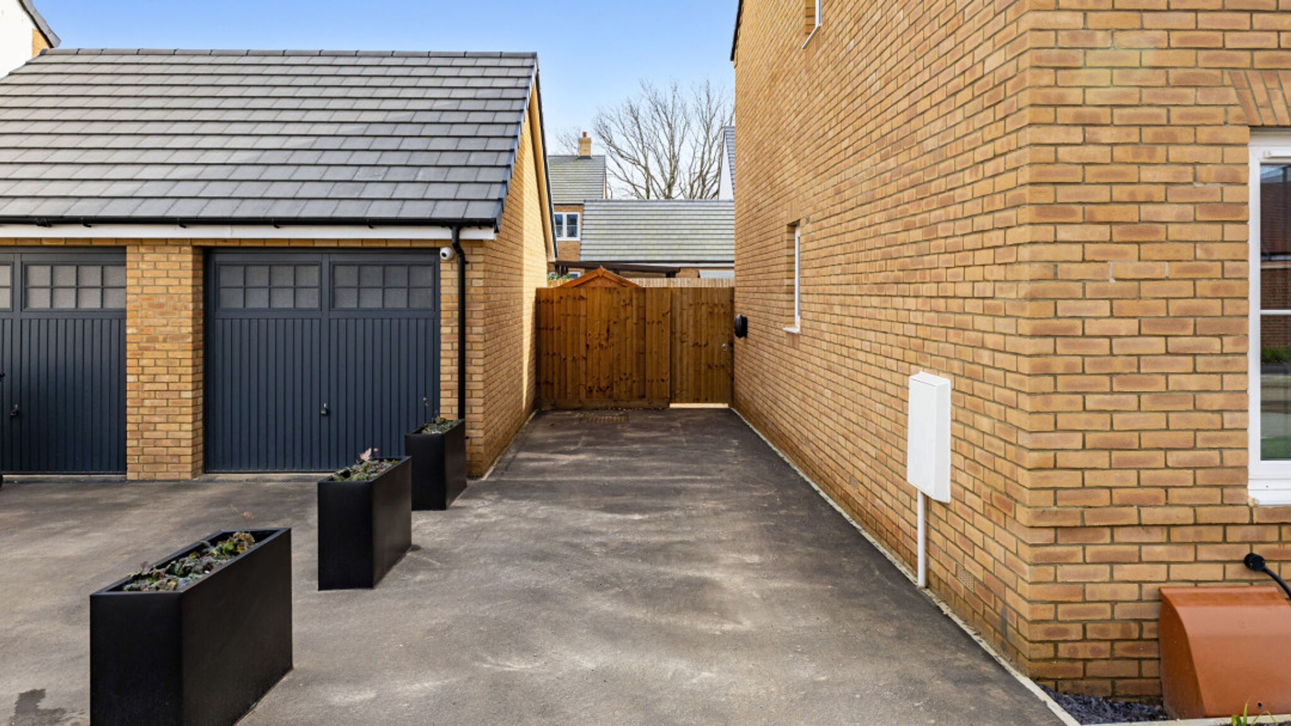 A driveway leading to a double garage with dark grey doors and a wooden gate.