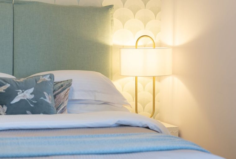 A bedroom with a bed, pillows, and a bedside lamp.