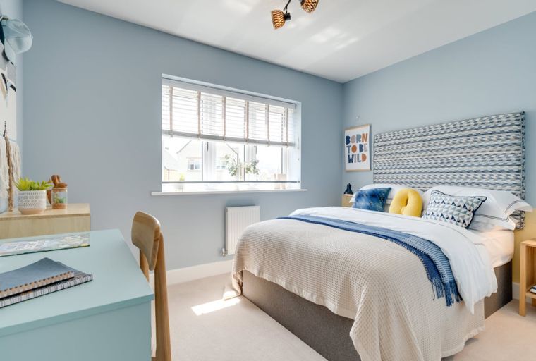 A bedroom with a bed, a desk, and a window.