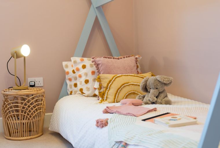 A child's bed with a teepee frame, pillows, a stuffed elephant, and a nightstand with a lamp.