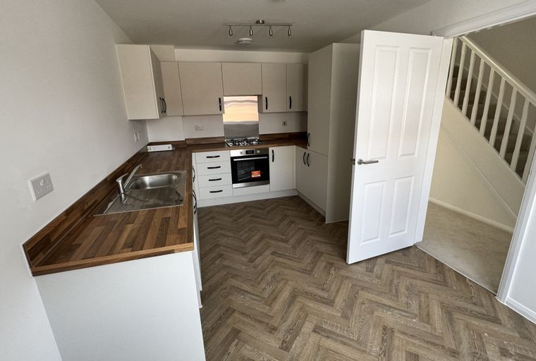 A kitchen with white cabinets, a wooden countertop, a sink, a gas hob, and an oven.