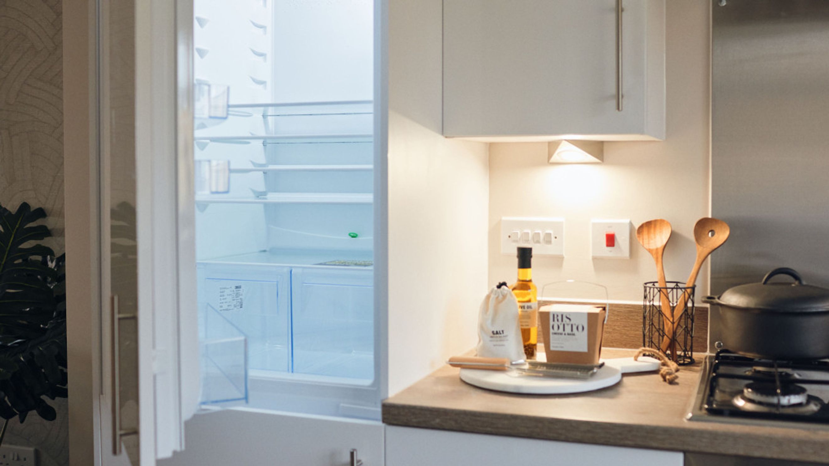 A kitchen counter with cooking utensils, a bottle of olive oil, and an open refrigerator.