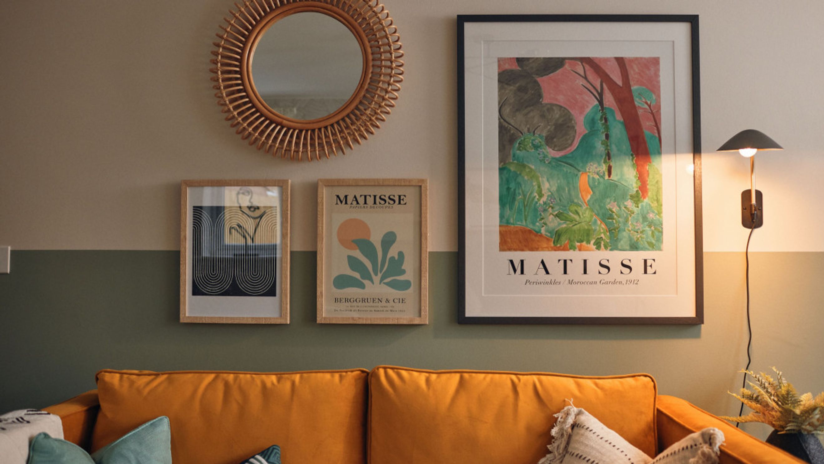 A living room with an orange sofa, framed art, and a wall lamp.