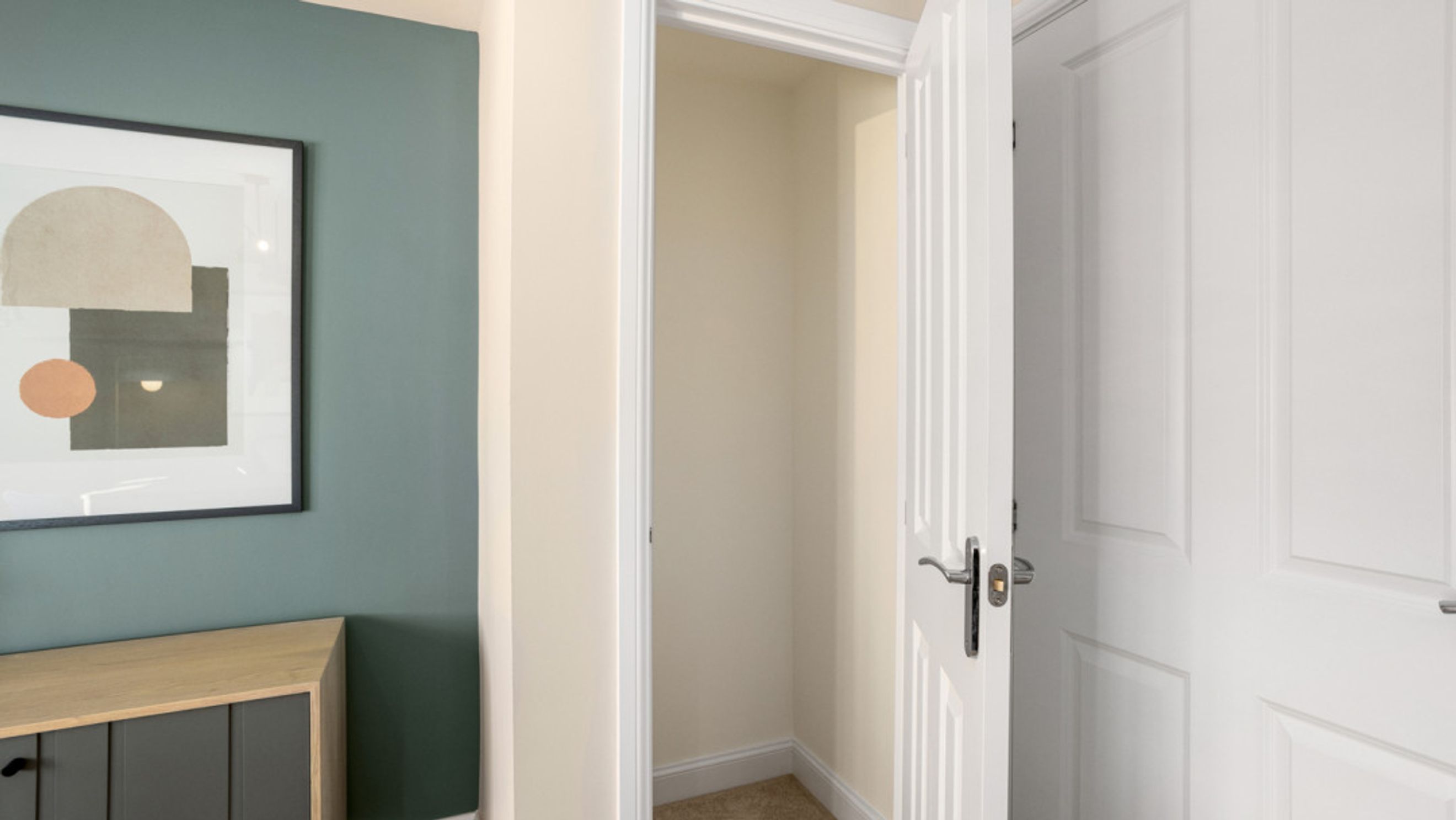A closet with an open door next to a wall with artwork and a cabinet.