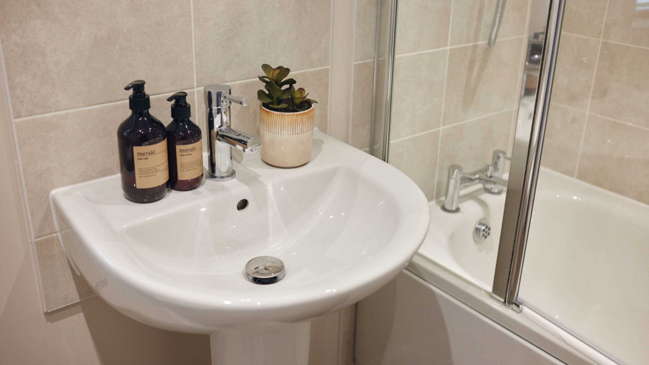 A bathroom sink with two soap dispensers, a faucet, and a small plant next to a bathtub.