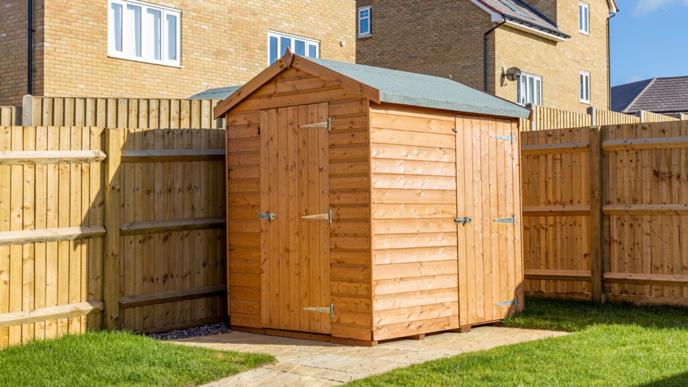 A wooden shed in a backyard with a wooden fence and grass.