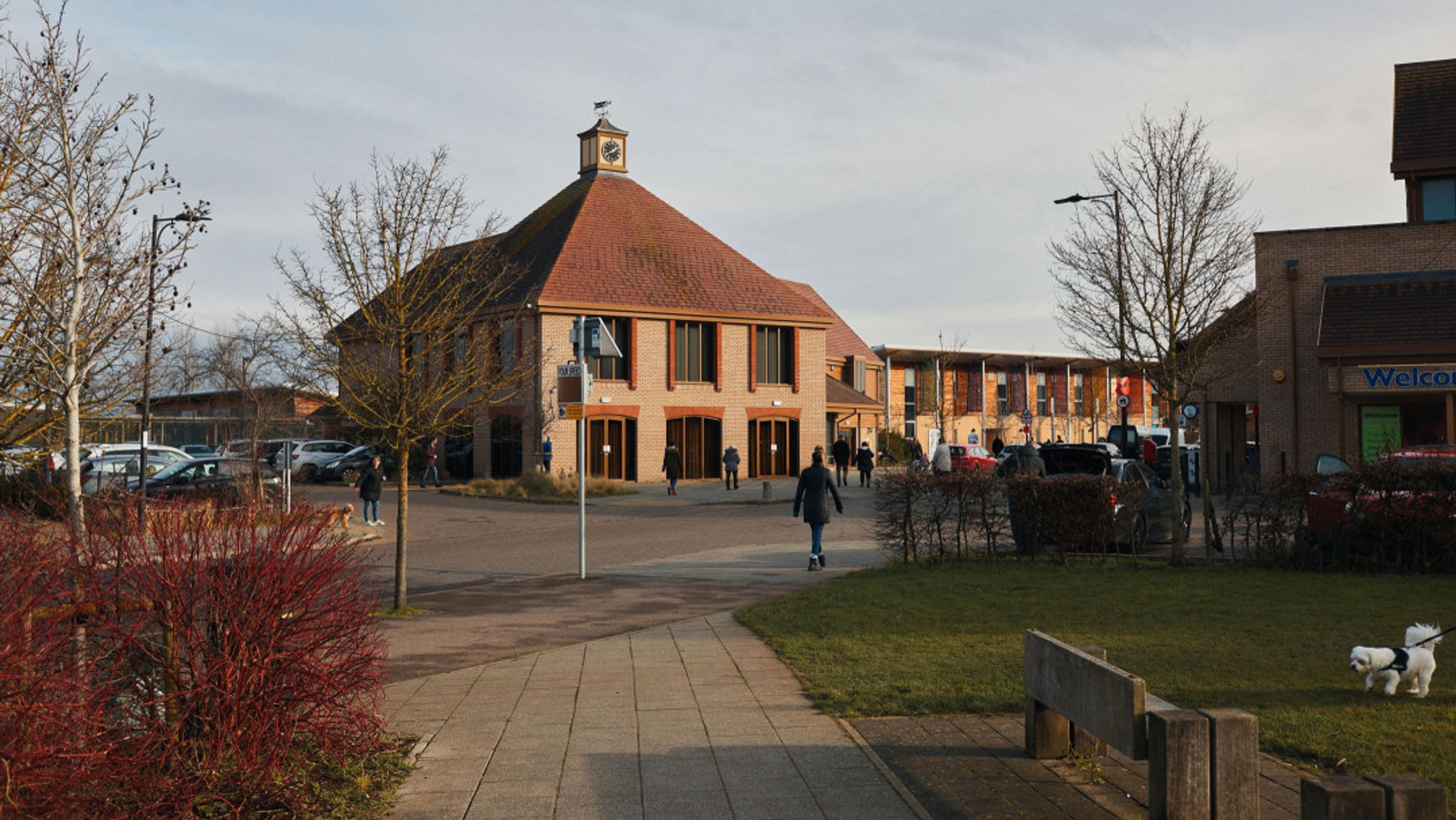 A brick building with a pitched roof and a clock tower, surrounded by trees and a parking lot.