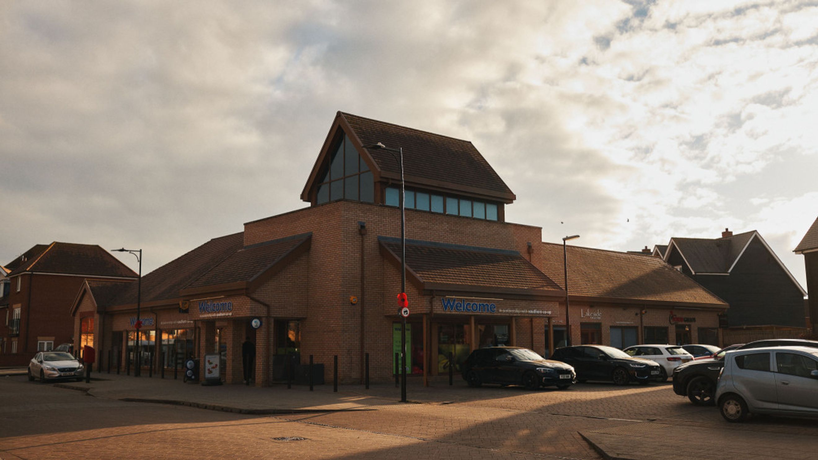 A brick commercial building with a pitched roof and a parking lot in front.