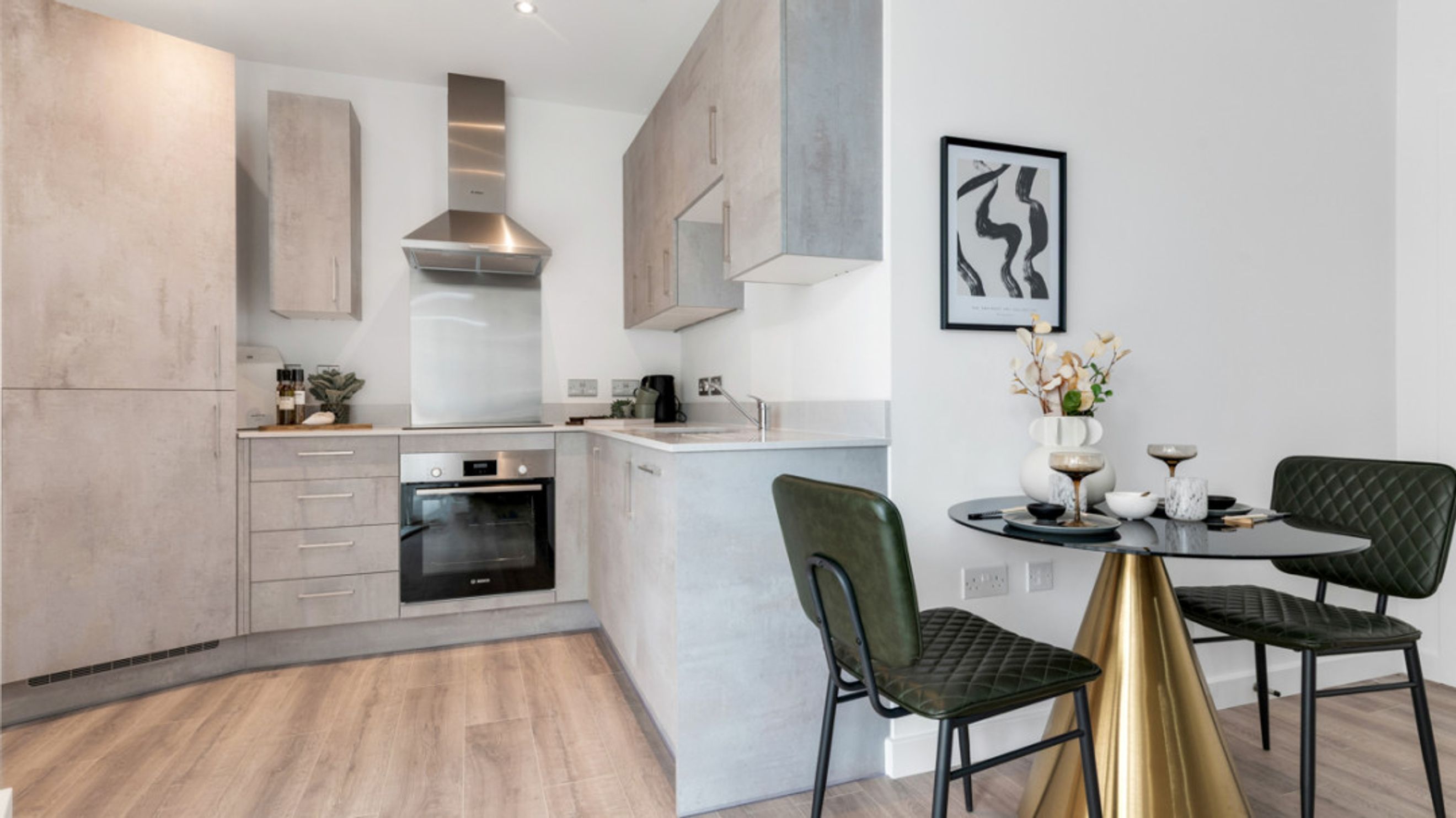 A modern kitchen and dining area with concrete-effect cabinets, an oven, a dining table, and two chairs.