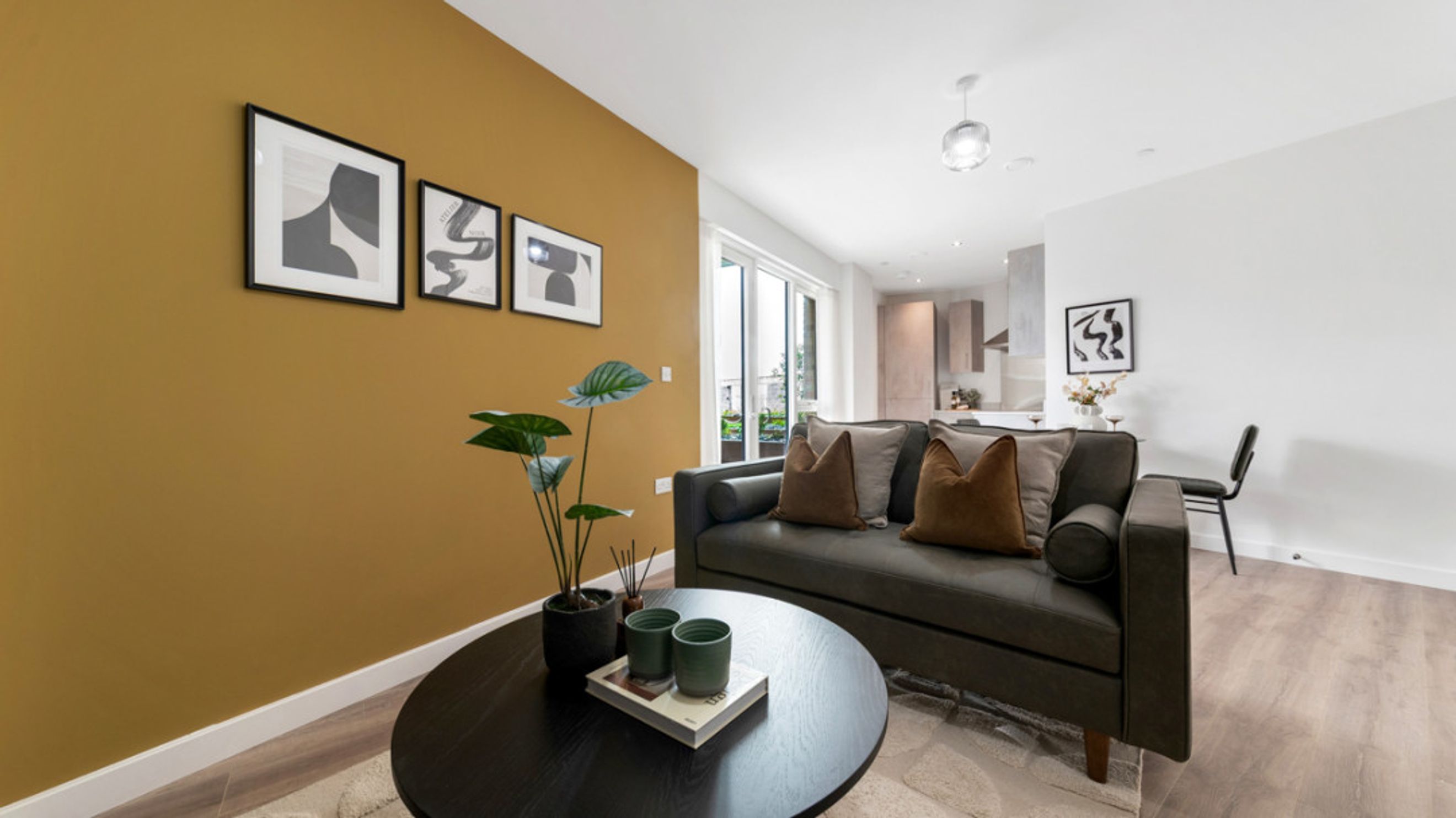 A living room with a sofa, coffee table, and artwork on a mustard-colored wall.