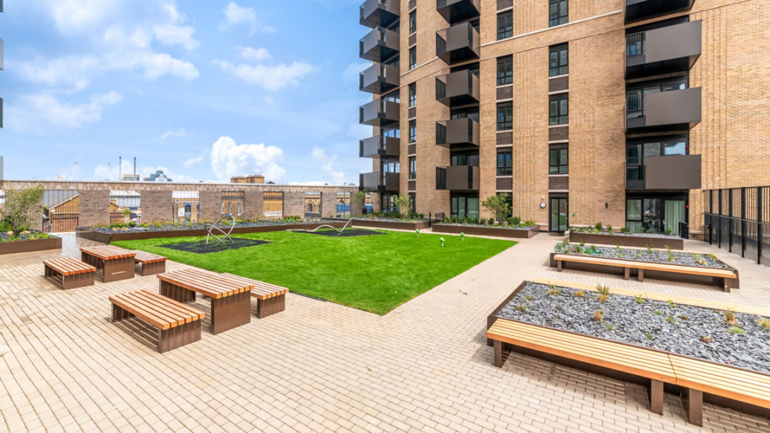 A rooftop terrace with a lawn, benches, and planters.