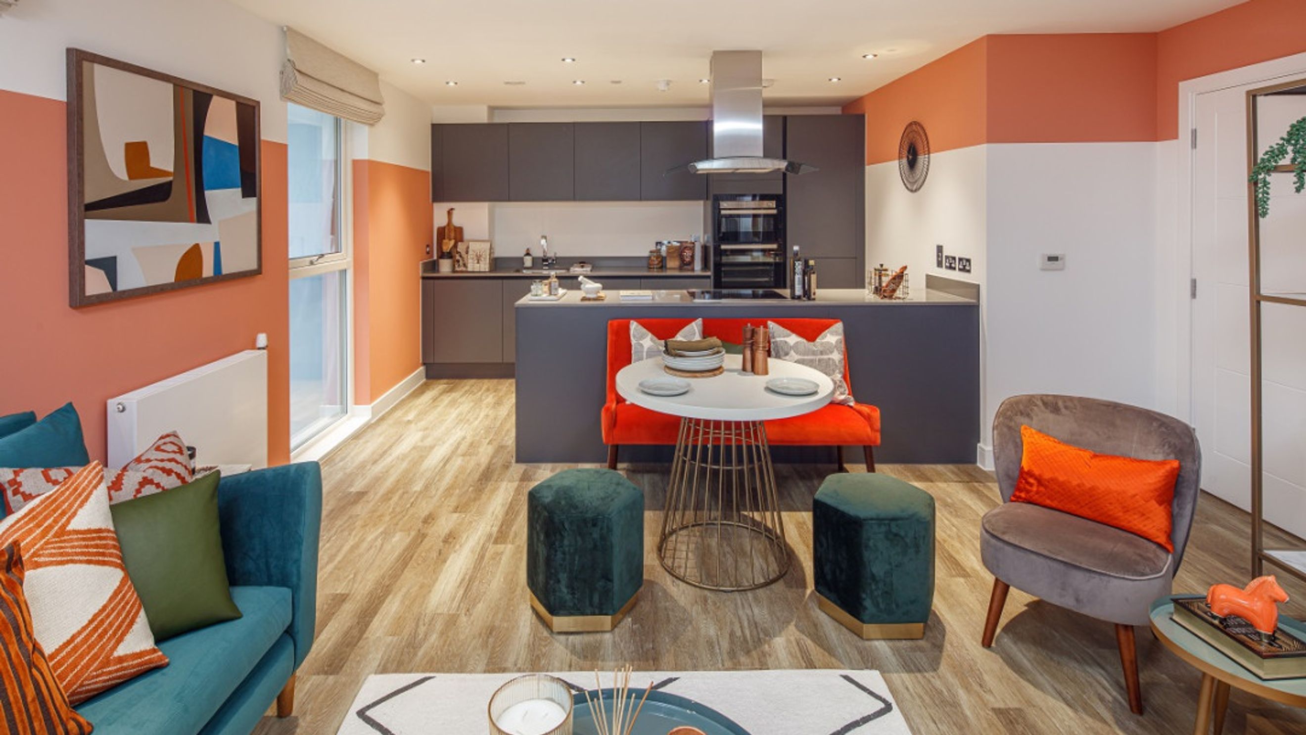 A modern open-plan living and kitchen area with a teal sofa, grey kitchen cabinets, and a dining set.