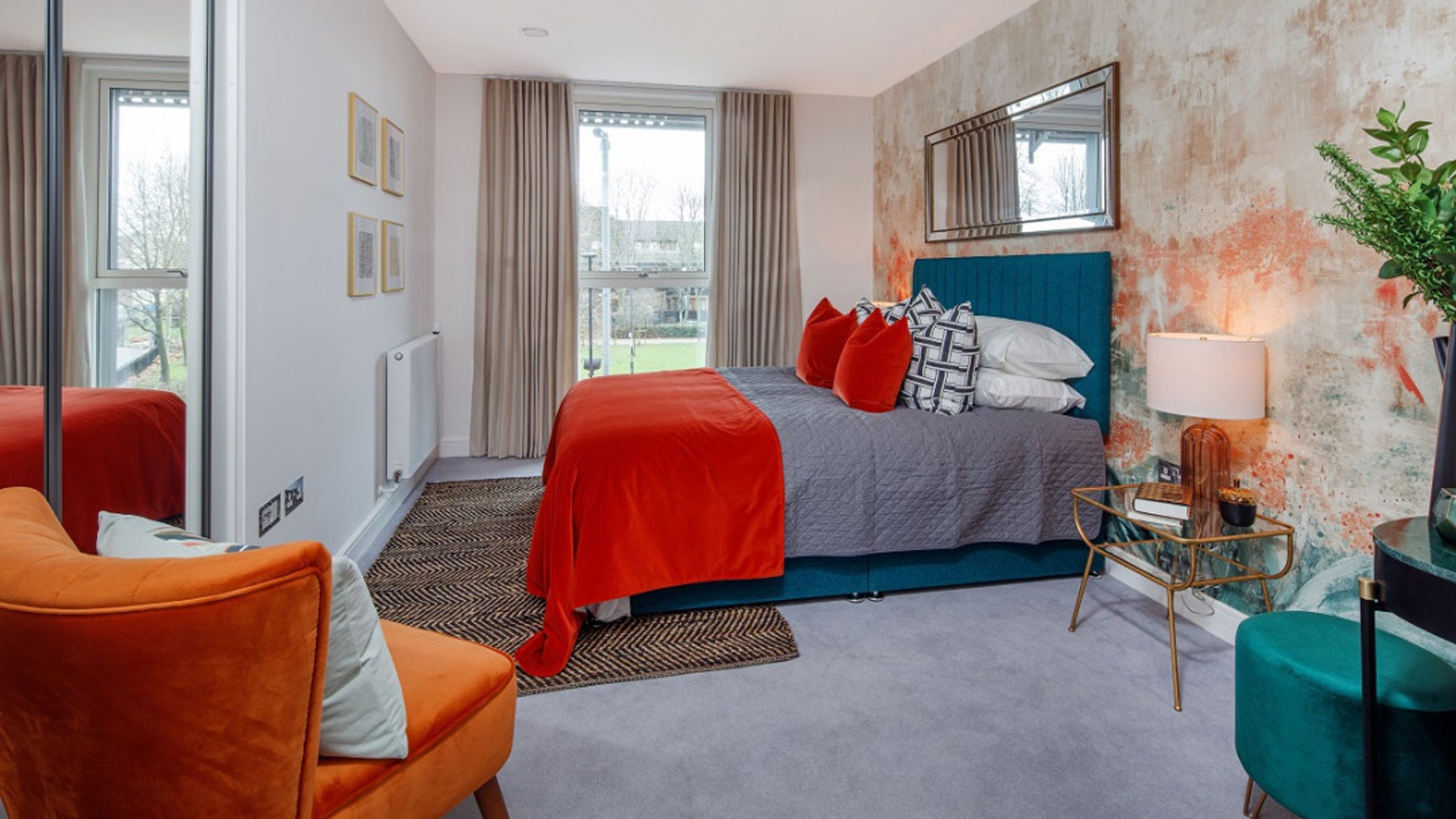 A bedroom with a bed, orange throw, and a bedside lamp.