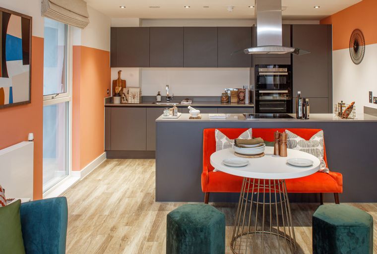 A modern kitchen and dining area with grey cabinets, an orange breakfast bar, and a round table.