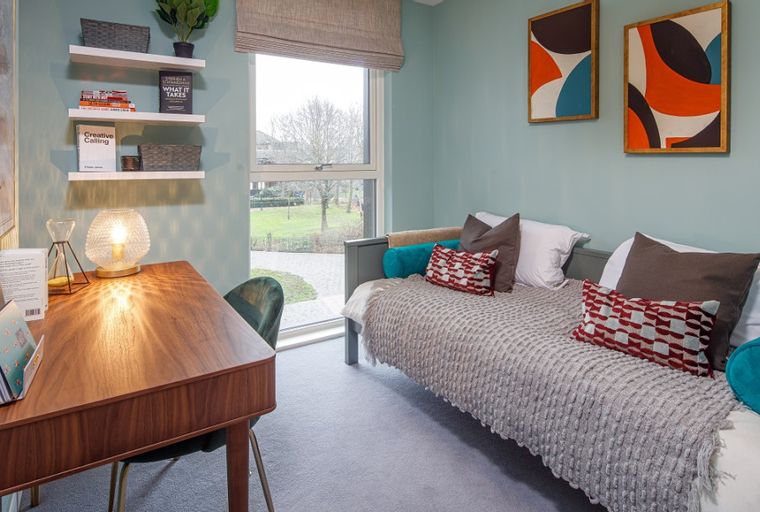 A bedroom with a daybed, desk, and window.