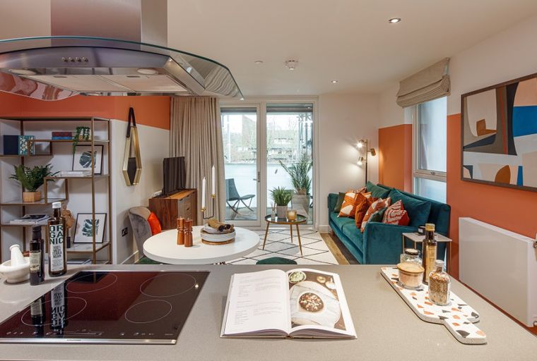 A modern apartment living area and kitchen with a teal sofa, dining table, and kitchen island.