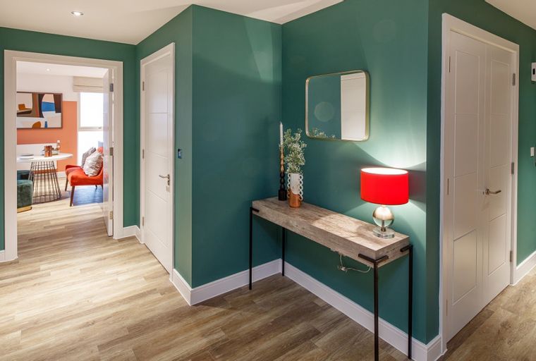 A hallway with teal walls, white doors, a console table with a lamp, and a view into a dining area.