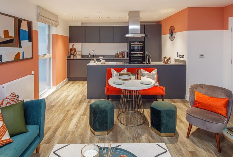 A modern open-plan living and kitchen area with a teal sofa, grey kitchen cabinets, and a dining set.