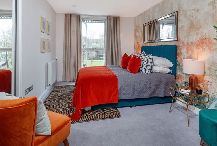 A bedroom with a bed, orange throw, and a bedside lamp.