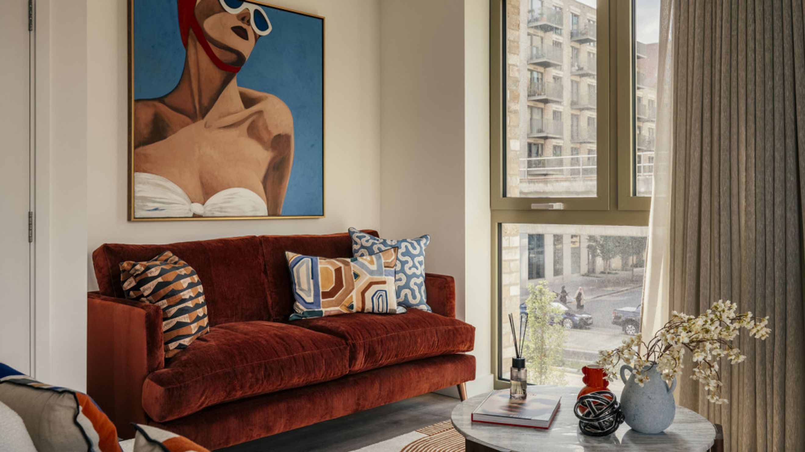 A living room with a rust-colored sofa, decorative pillows, and a large painting.