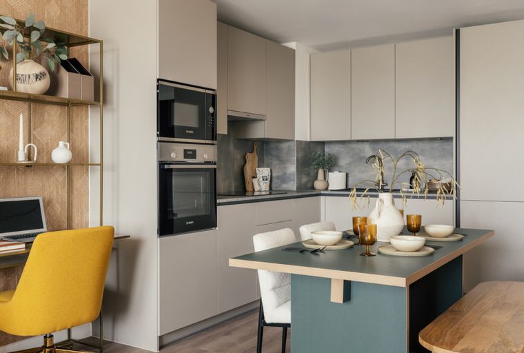 A modern kitchen and dining area with a built-in oven and microwave, a dining table with chairs, and a small desk with a laptop.