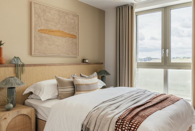 A bedroom with a bed, pillows, a headboard, bedside tables, lamps, and a window with curtains.