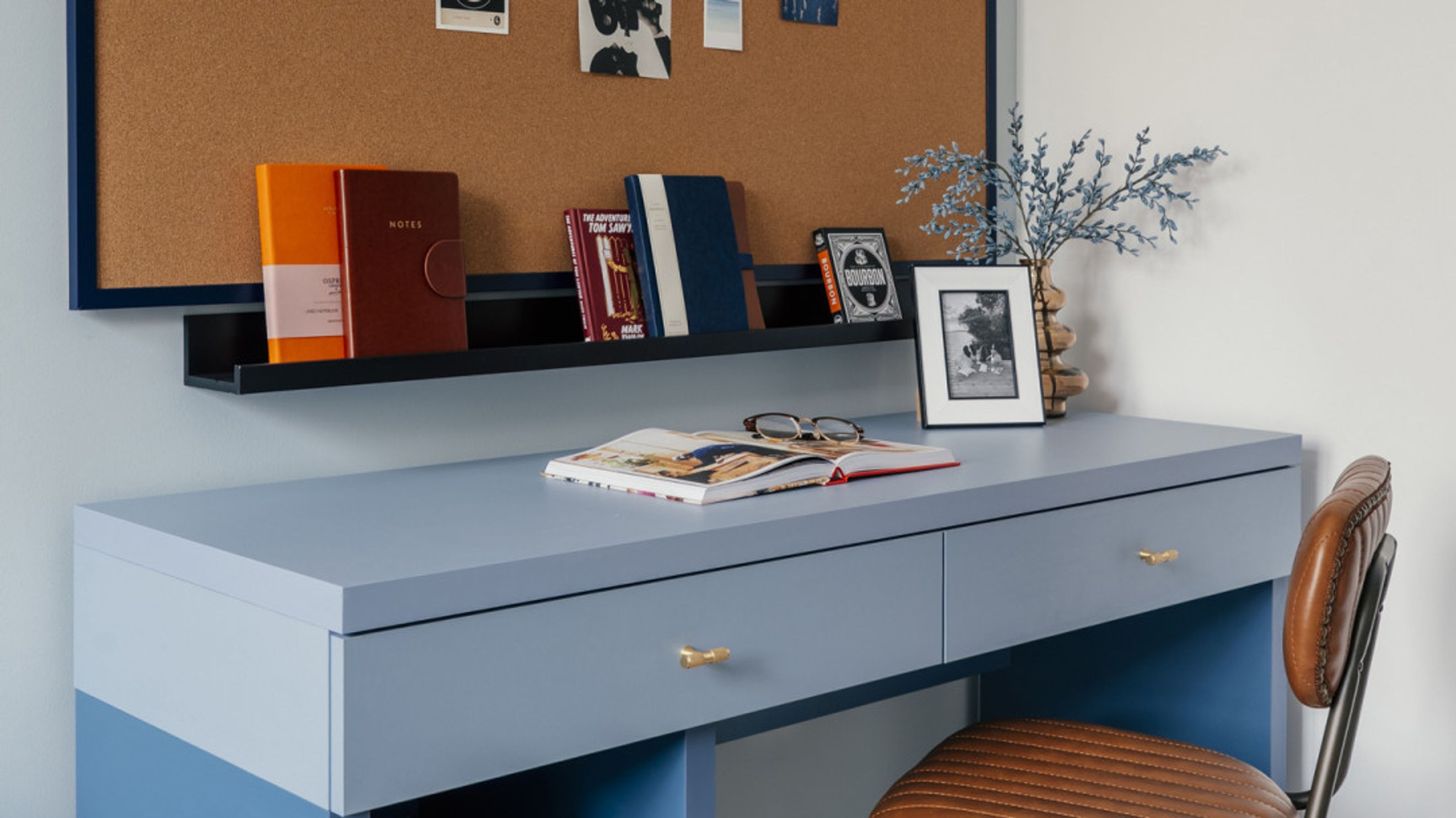 A blue desk with books, glasses, and a framed photo on top.